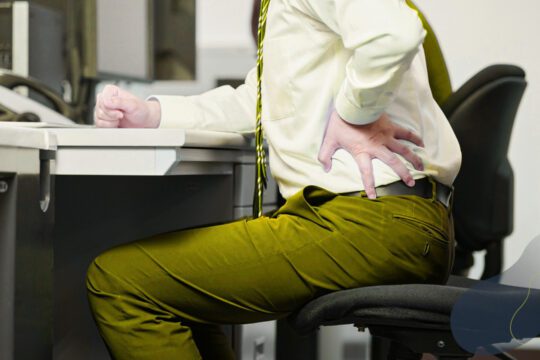 Osoba siedząca przy biurku, odczuwająca ból dolnej części pleców. Ilustracja przedstawia temat pracy z bólem w hipnoterapii.