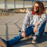 Mężczyzna siedzący na deskorolce na miejskim nabrzeżu, w swobodnej i niezależnej postawie.