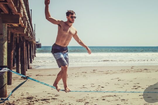 Mężczyzna idący po linie na plaży, utrzymujący równowagę ciała w ruchu.