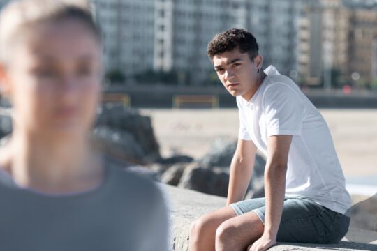 Mężczyzna siedzący na murku patrzy w stronę oddalającej się kobiety - symbol trudnych emocji po rozstaniu