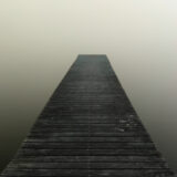 Poczucie pustki - samotny pomost na szarym tle znikający we mgle jako obraz obojętnej rzeczywistości